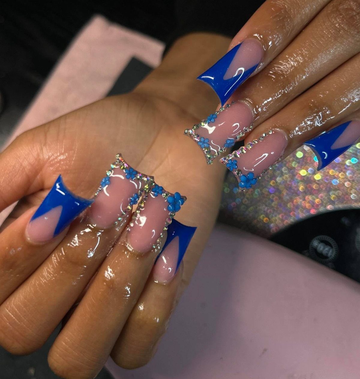 Long acrylic nails with deep blue polish, silver glitter, and blue floral accents.
