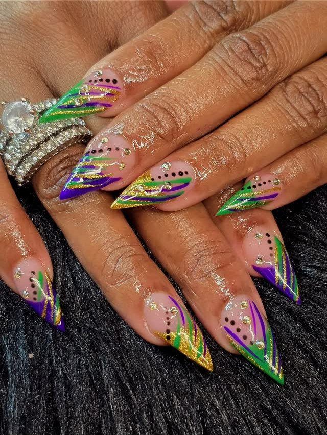Stiletto nails with purple, green, and gold glitter swirls and dot accents.
