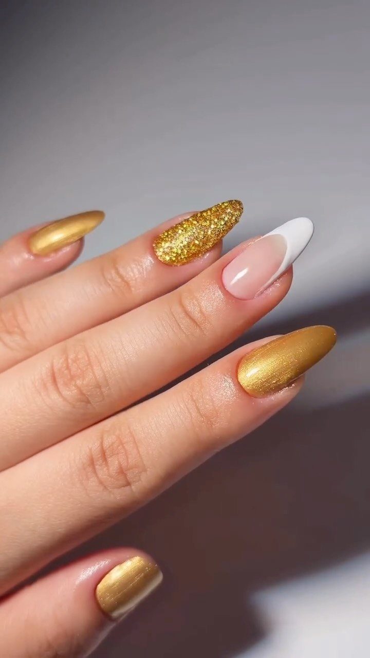 Hand with almond nails in metallic gold, gold glitter, and white French tip.