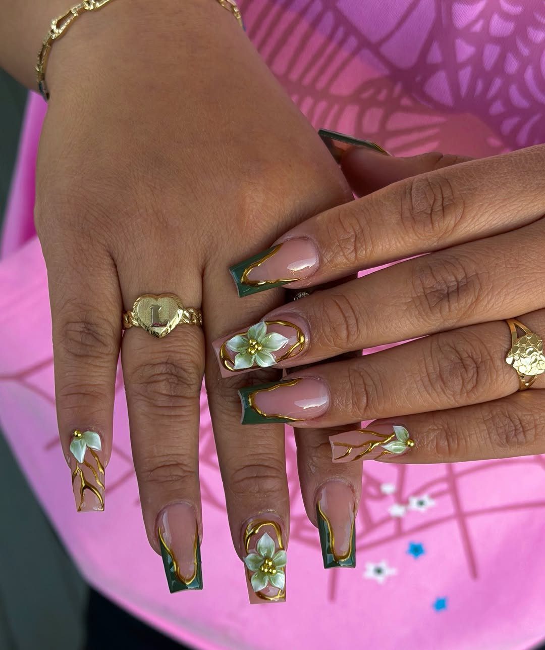 Long coffin nails with dark green polish, gold accents, and 3D white flowers.