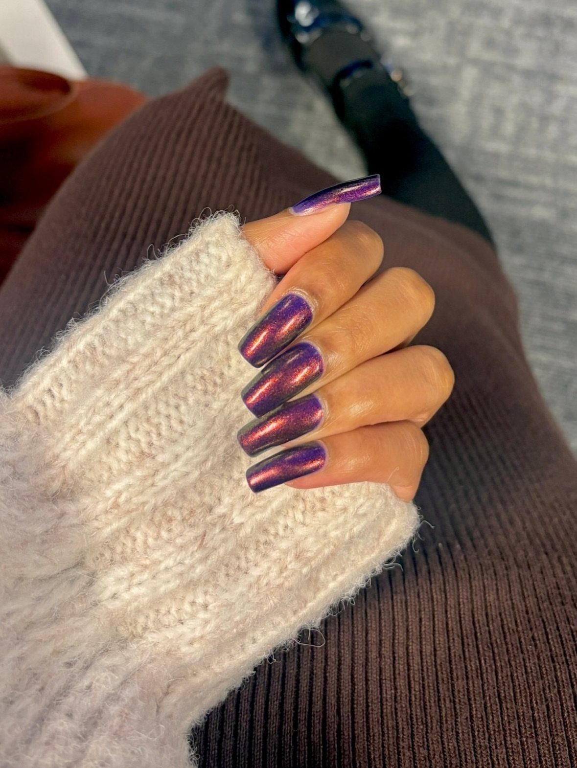 Long coffin nails with iridescent purple and gold metallic polish on a hand.