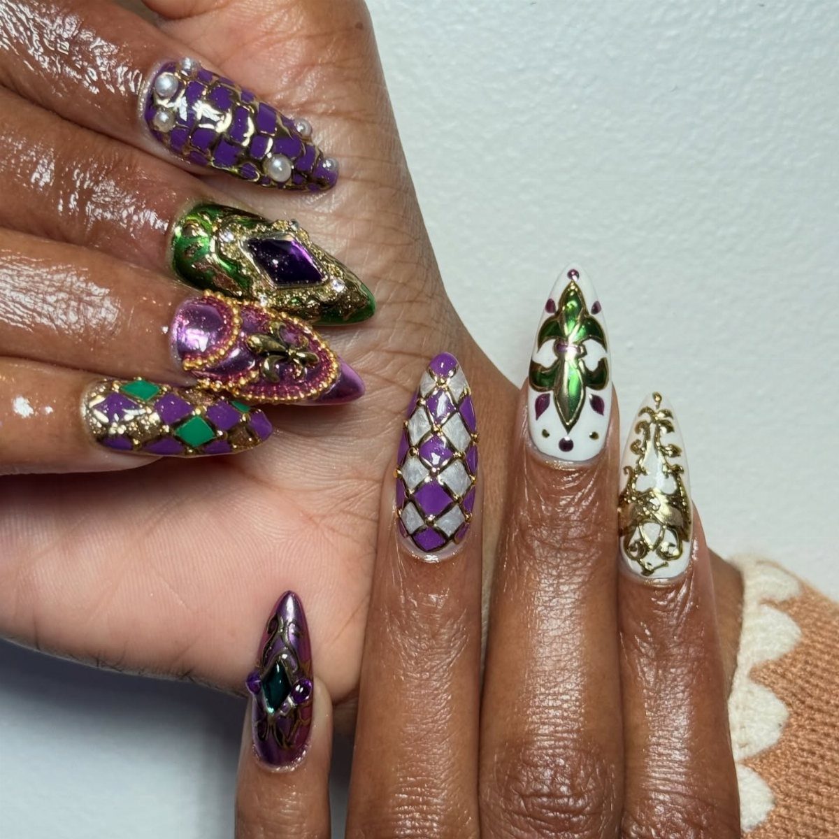 Stiletto nails with purple, green, and gold designs featuring 3D gold beads and pearls.