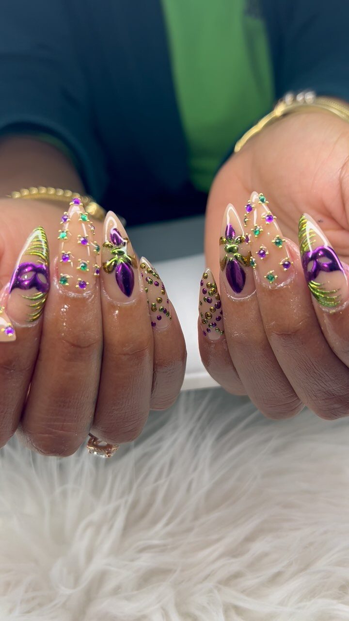 Stiletto nails with purple, green, and gold masquerade mask nail art and glitter.