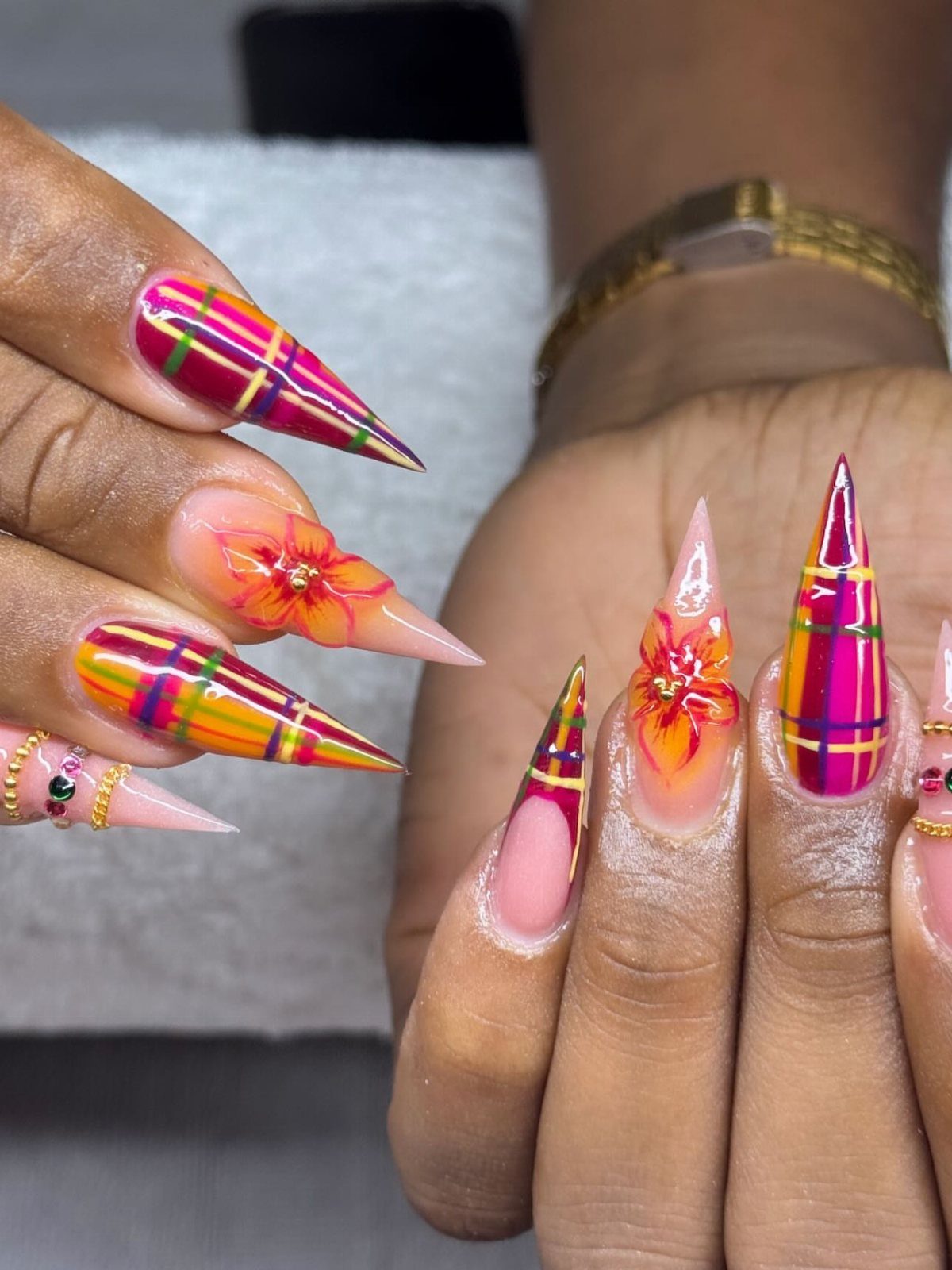 Stiletto nails with purple, green, and yellow plaid patterns and floral nail art.