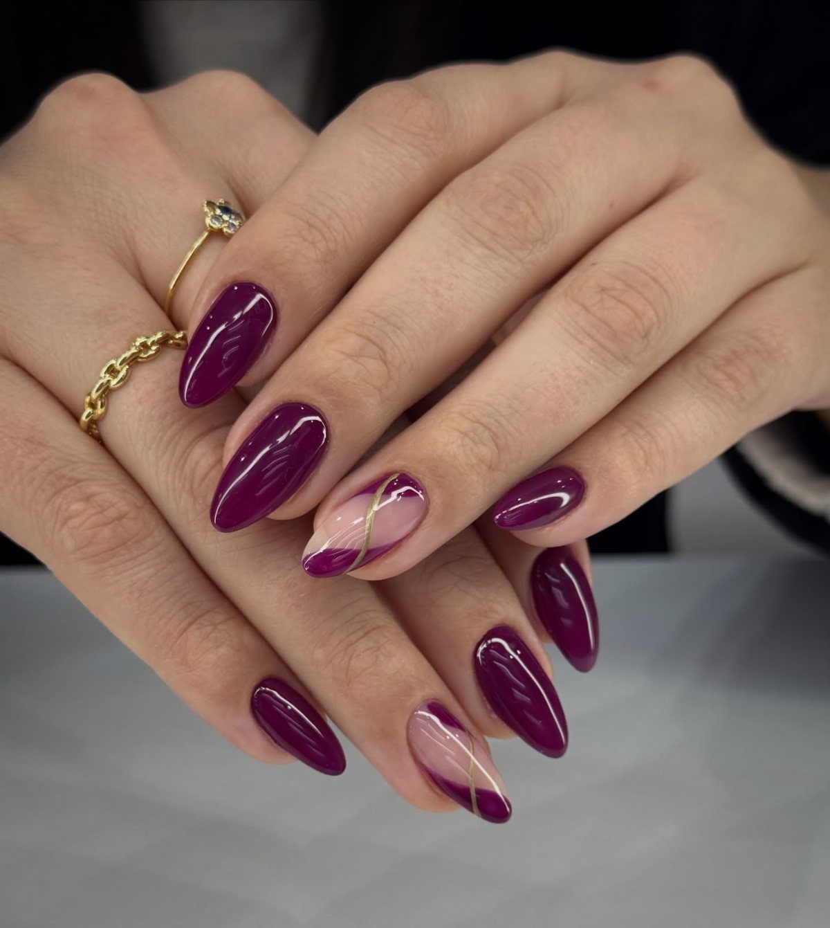 Deep purple almond-shaped nails with gold metallic accents on a person's hands.