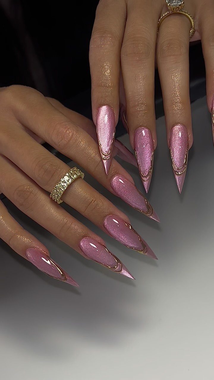 Long purple glitter stiletto nails with gold metallic accents and gold rings.