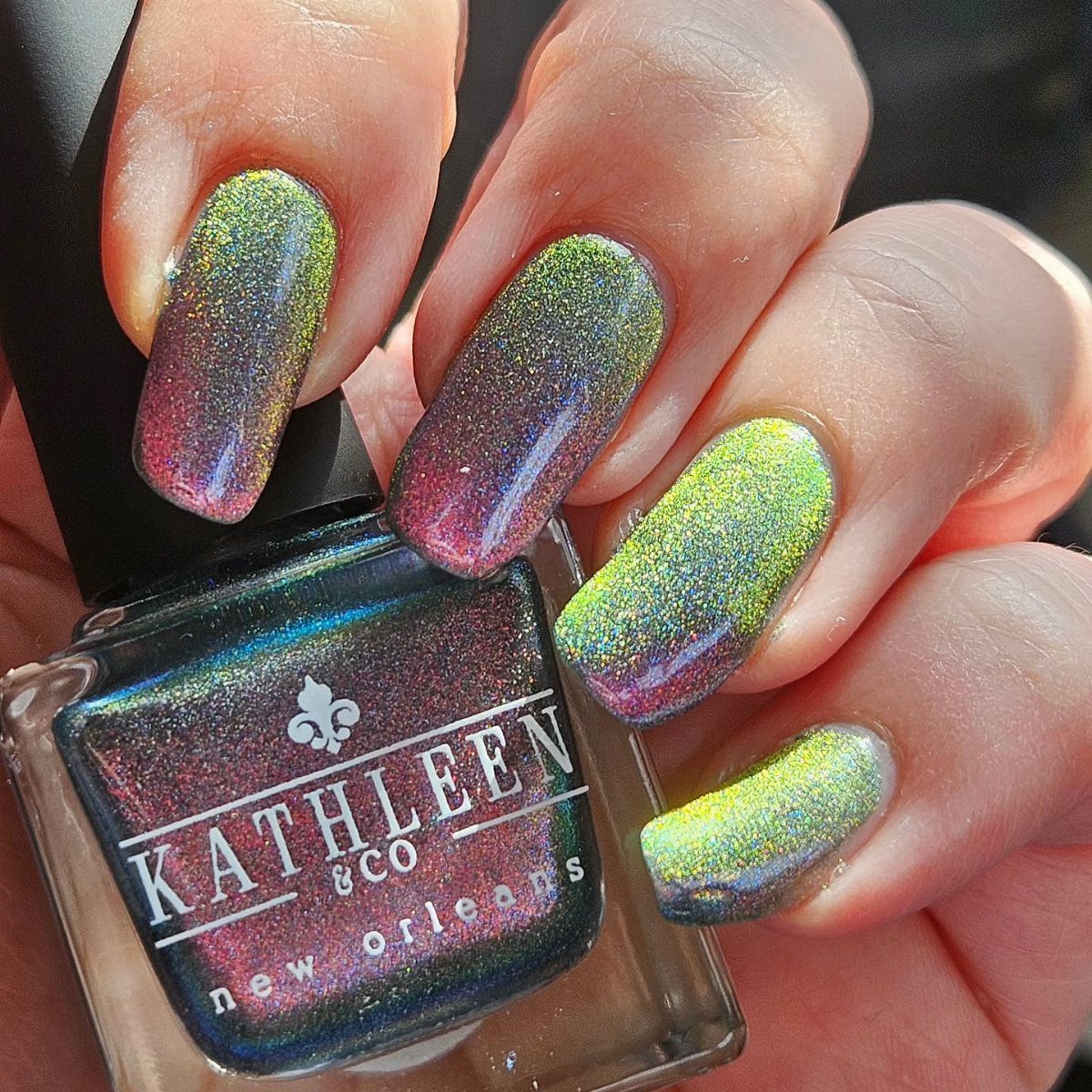 Holographic purple and green gradient nails holding a bottle of New Orleans polish.
