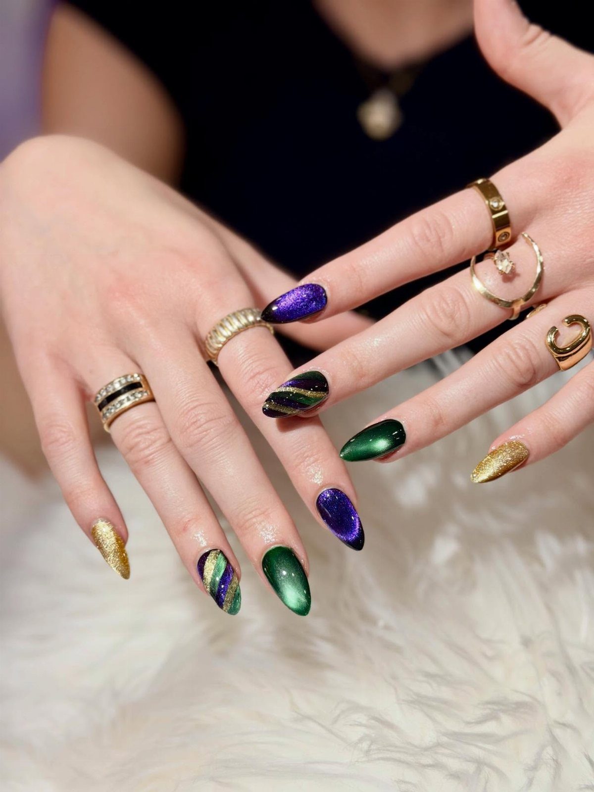 Hands with long almond nails in purple, green, and gold glitter colors.
