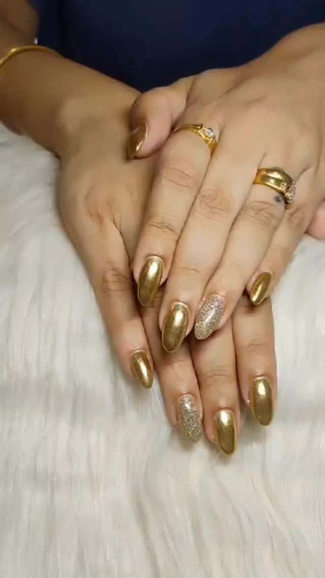Hands with gold metallic and glittery nail polish and gold rings on white fabric