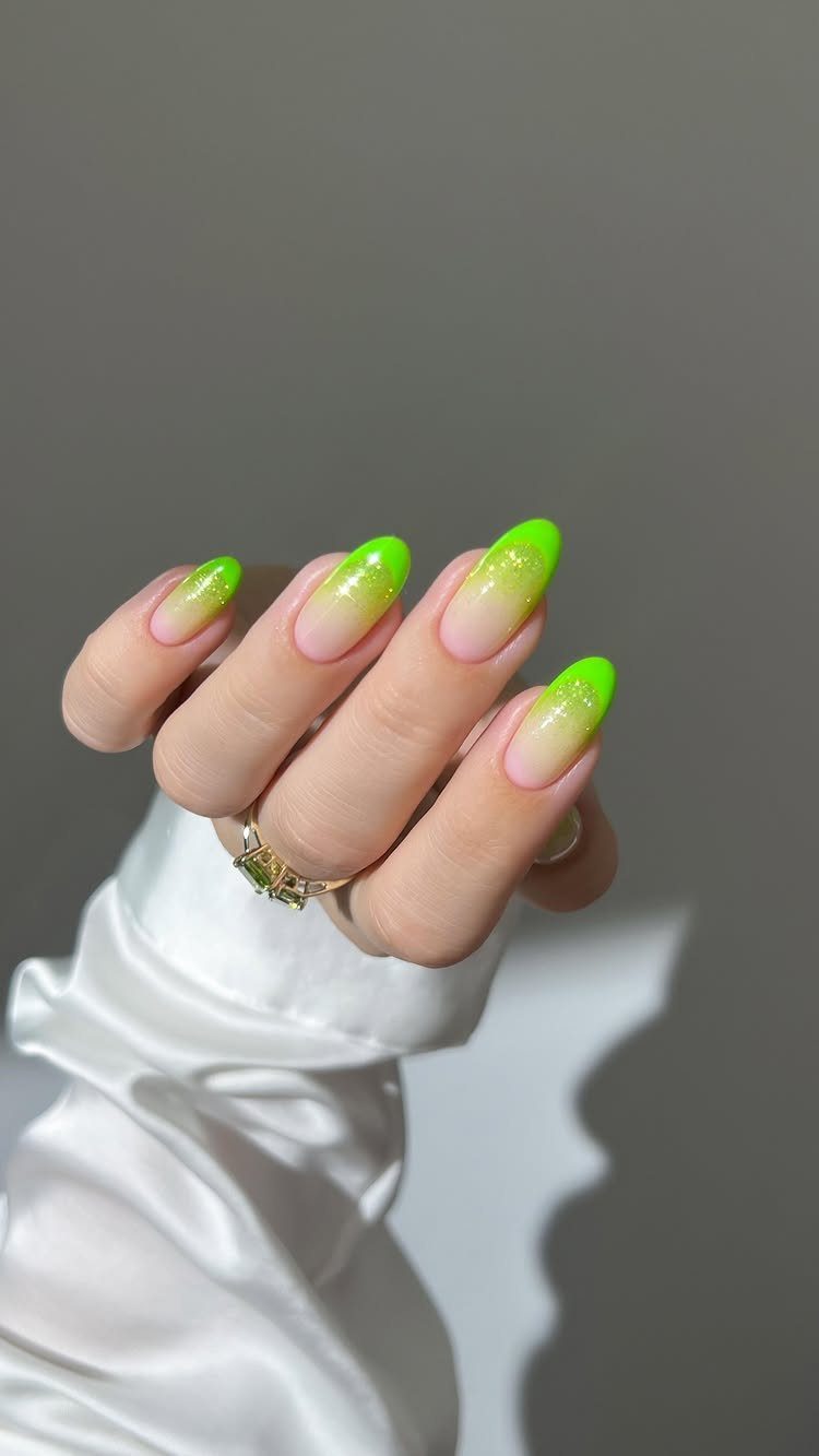 Hand with almond nails featuring a neon green glitter ombre gradient design.