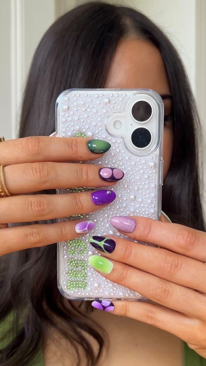 Manicured nails in purple and green shades holding a white beaded phone case.