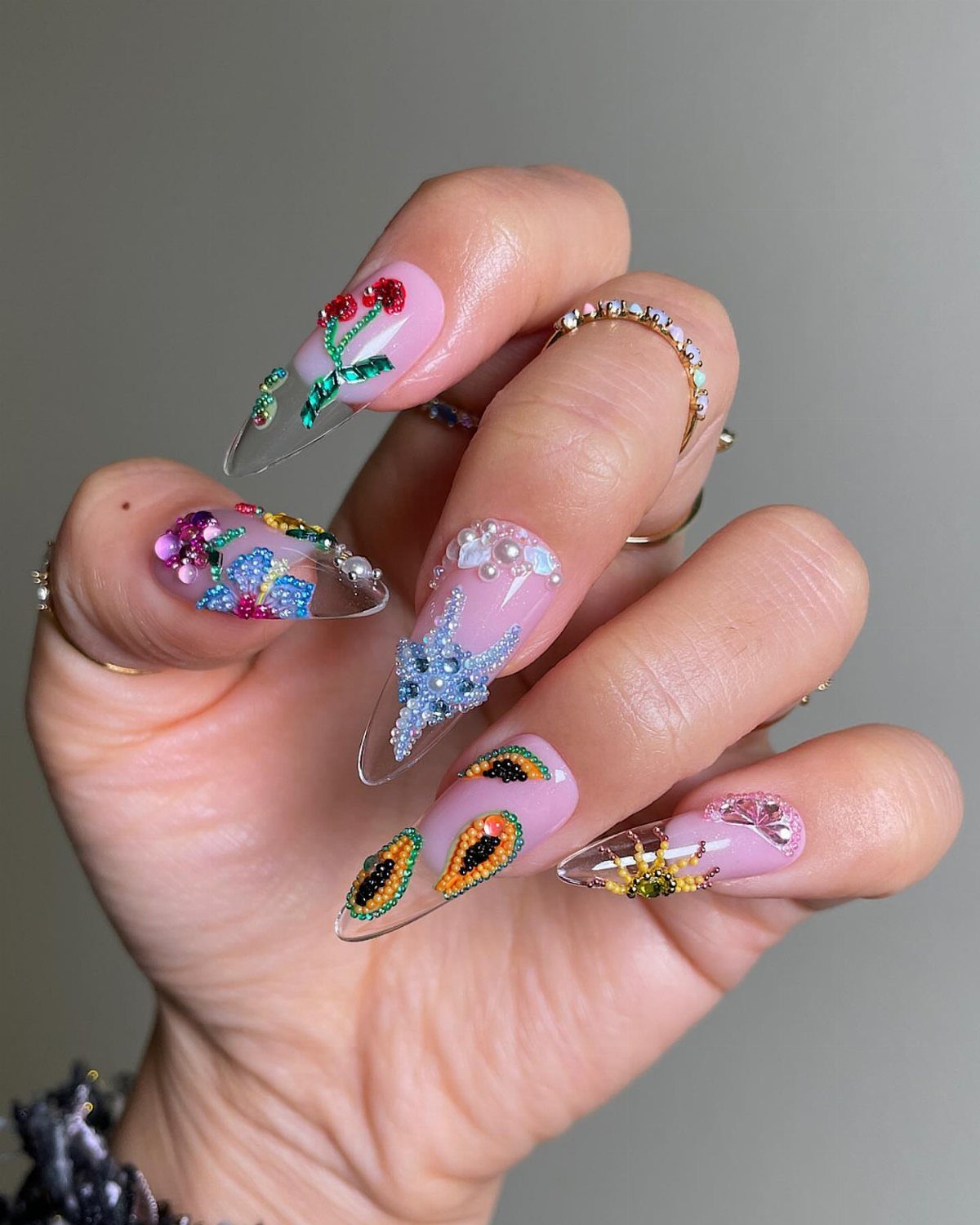 Long almond nails decorated with colorful jewels, pearls, and detailed 3D nail art.