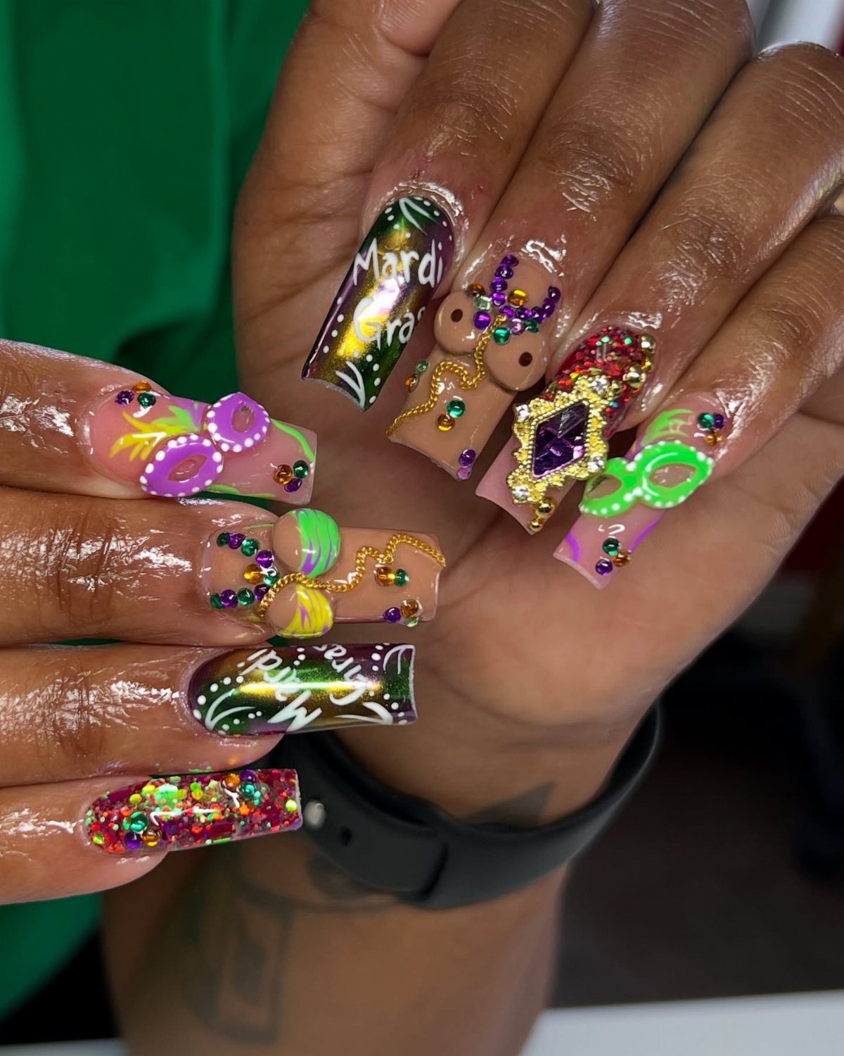 Intricate Mardi Gras nail art with purple, green, and gold rhinestones and lettering.