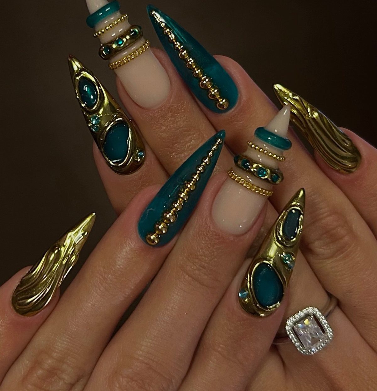 Long pointed nails with teal and gold 3D bead and metallic designs.