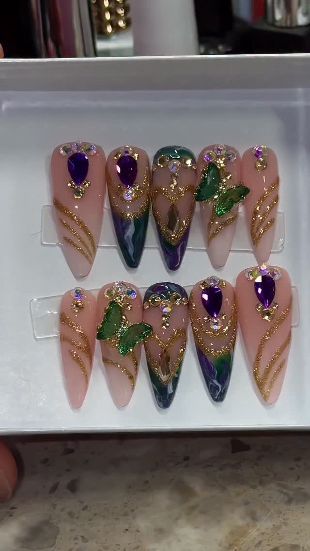 Stiletto artificial nails with purple, green, and gold Mardi Gras themed nail art.