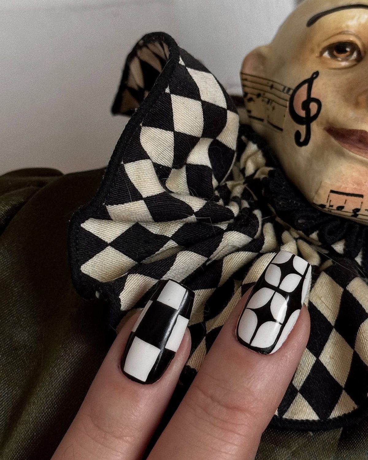 Black and white patterned nails next to a checkered jester collar and mask.