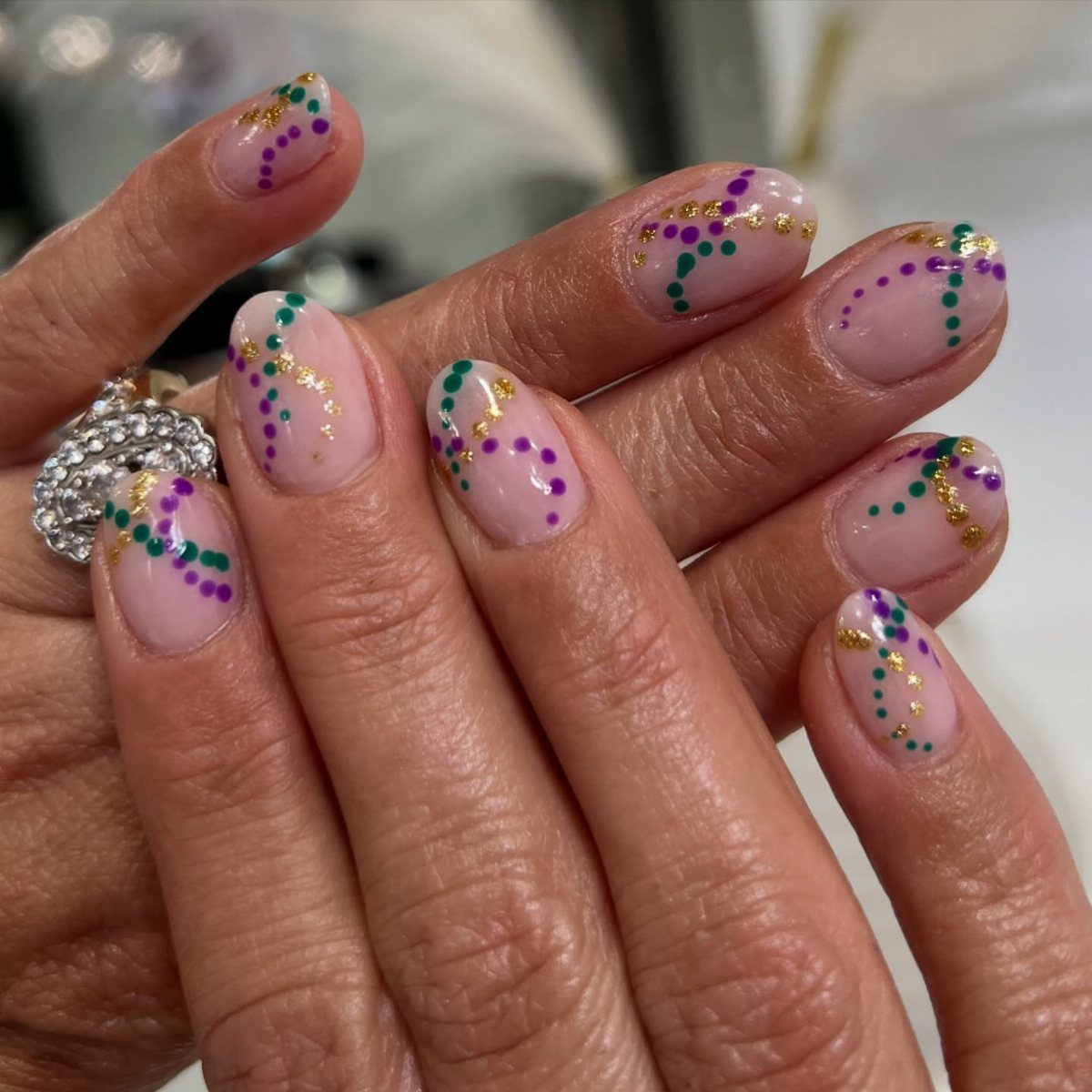 Natural nails with wavy lines of purple, green, and gold glitter dots.