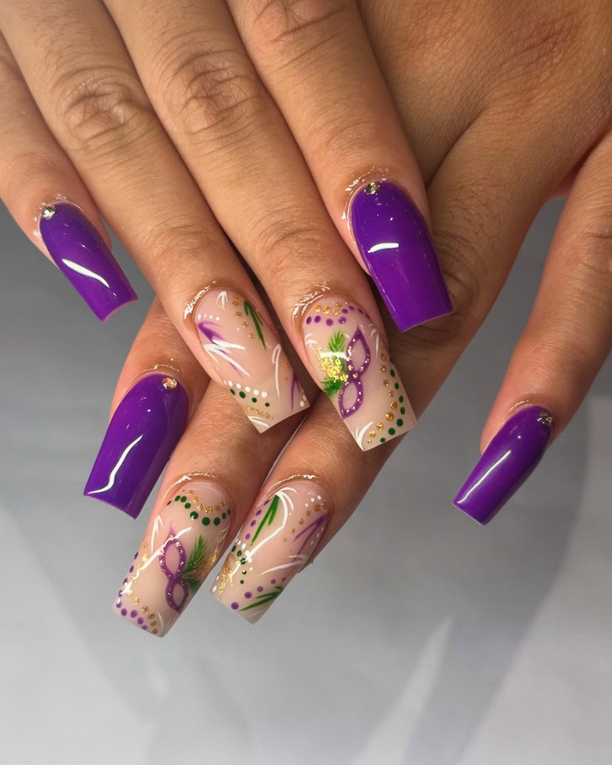 Long coffin nails with purple polish and painted gold and green masquerade masks.
