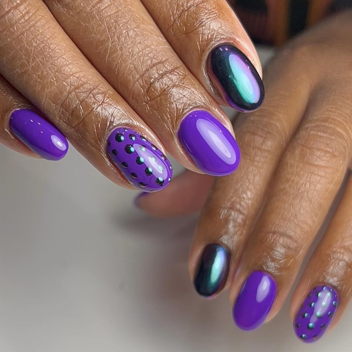 Purple and iridescent green nails with small gold and green polka dots.