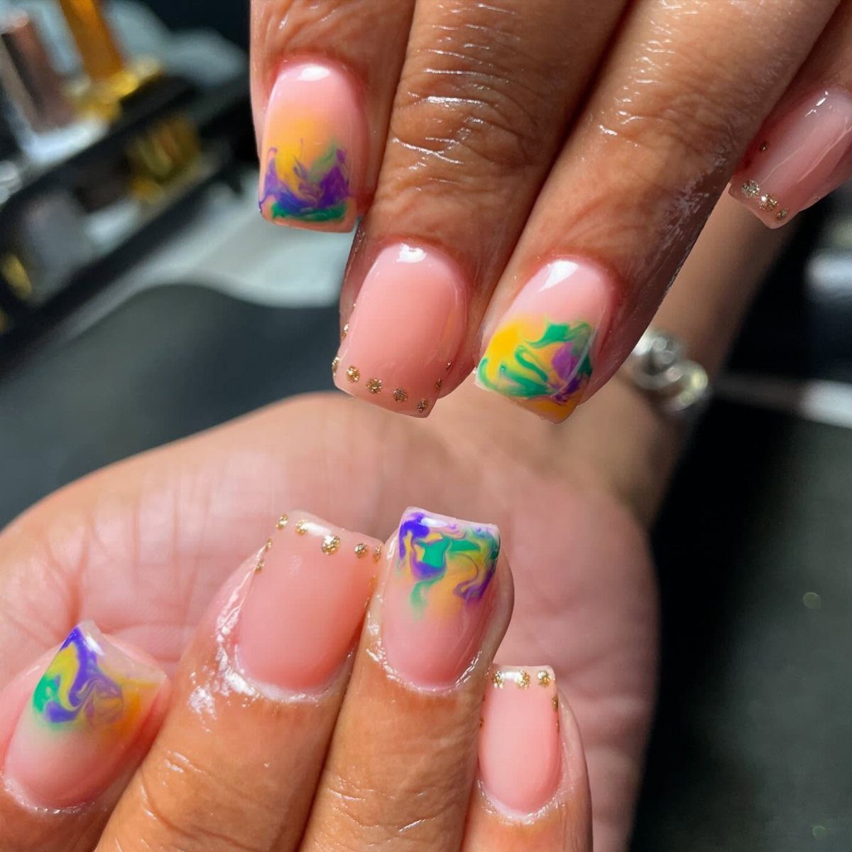 Manicured nails featuring purple, green, and gold swirled water marble nail art designs.