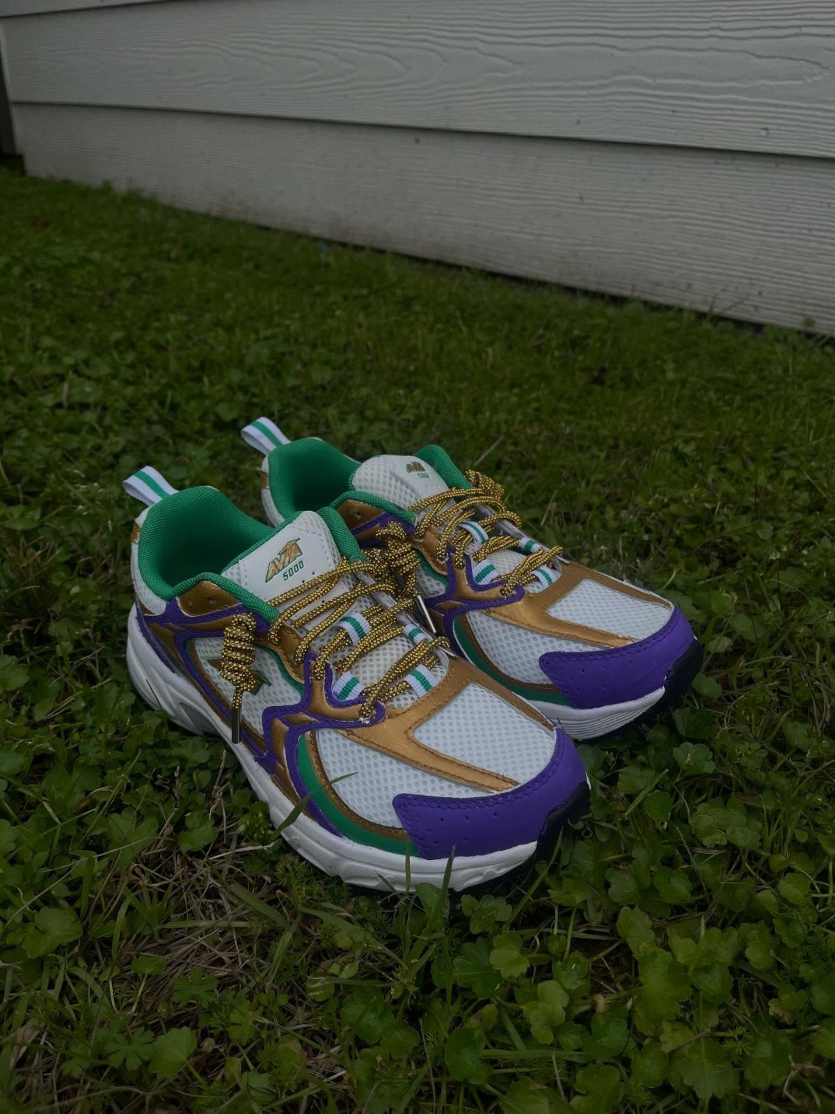 Purple, green, and gold athletic sneakers with gold laces on green grass.