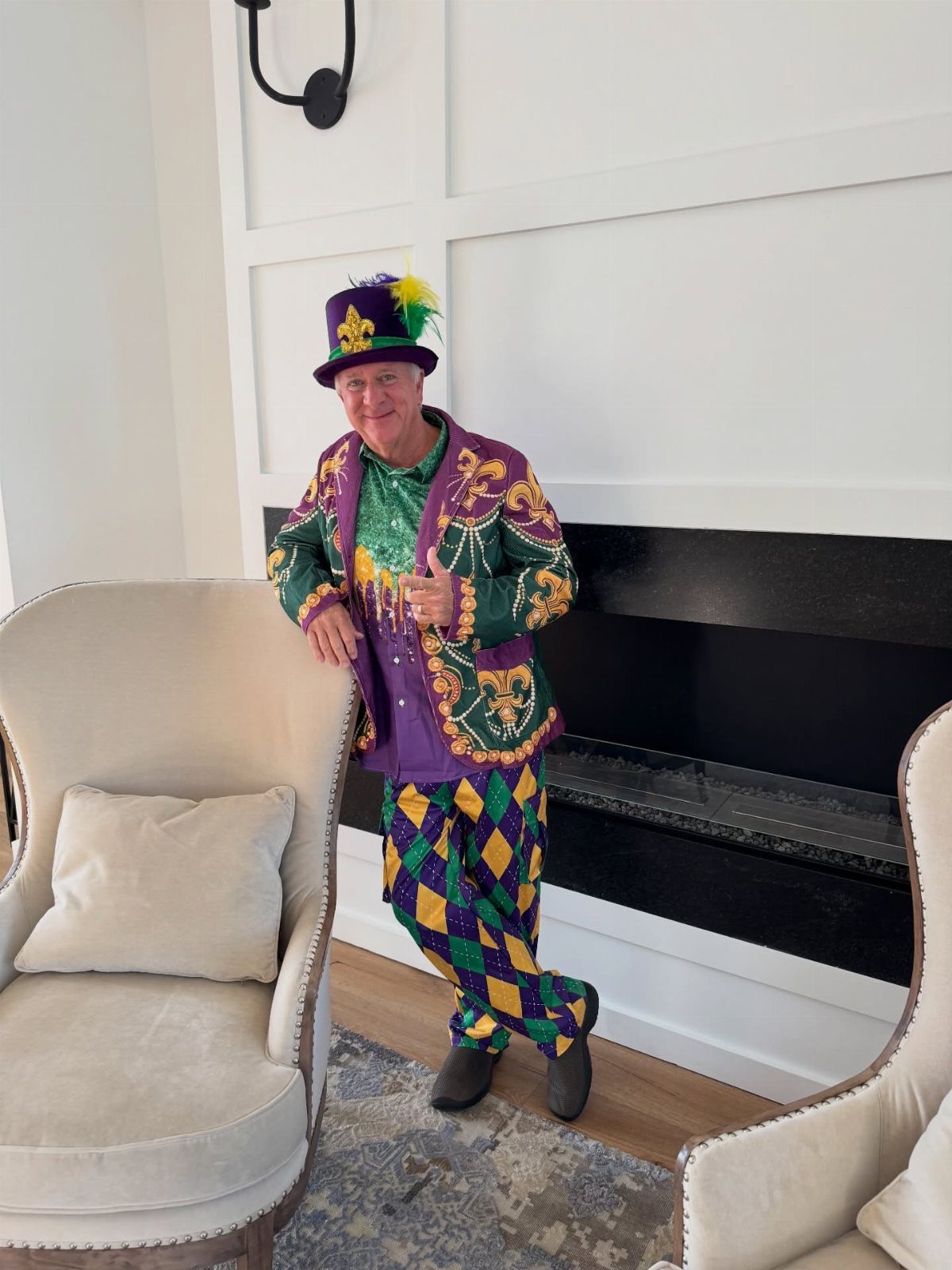 Man in a purple, green, and gold Mardi Gras costume standing in a living room.