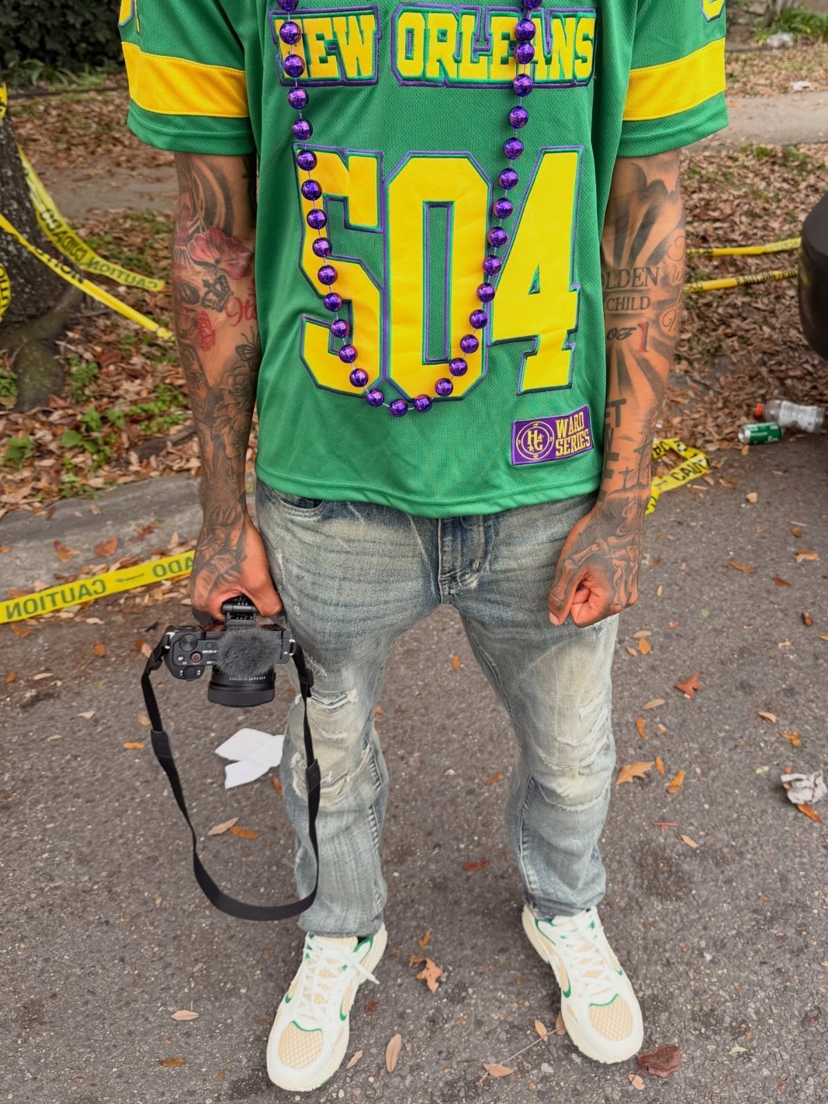 Man in New Orleans jersey and Mardi Gras beads holding a professional camera