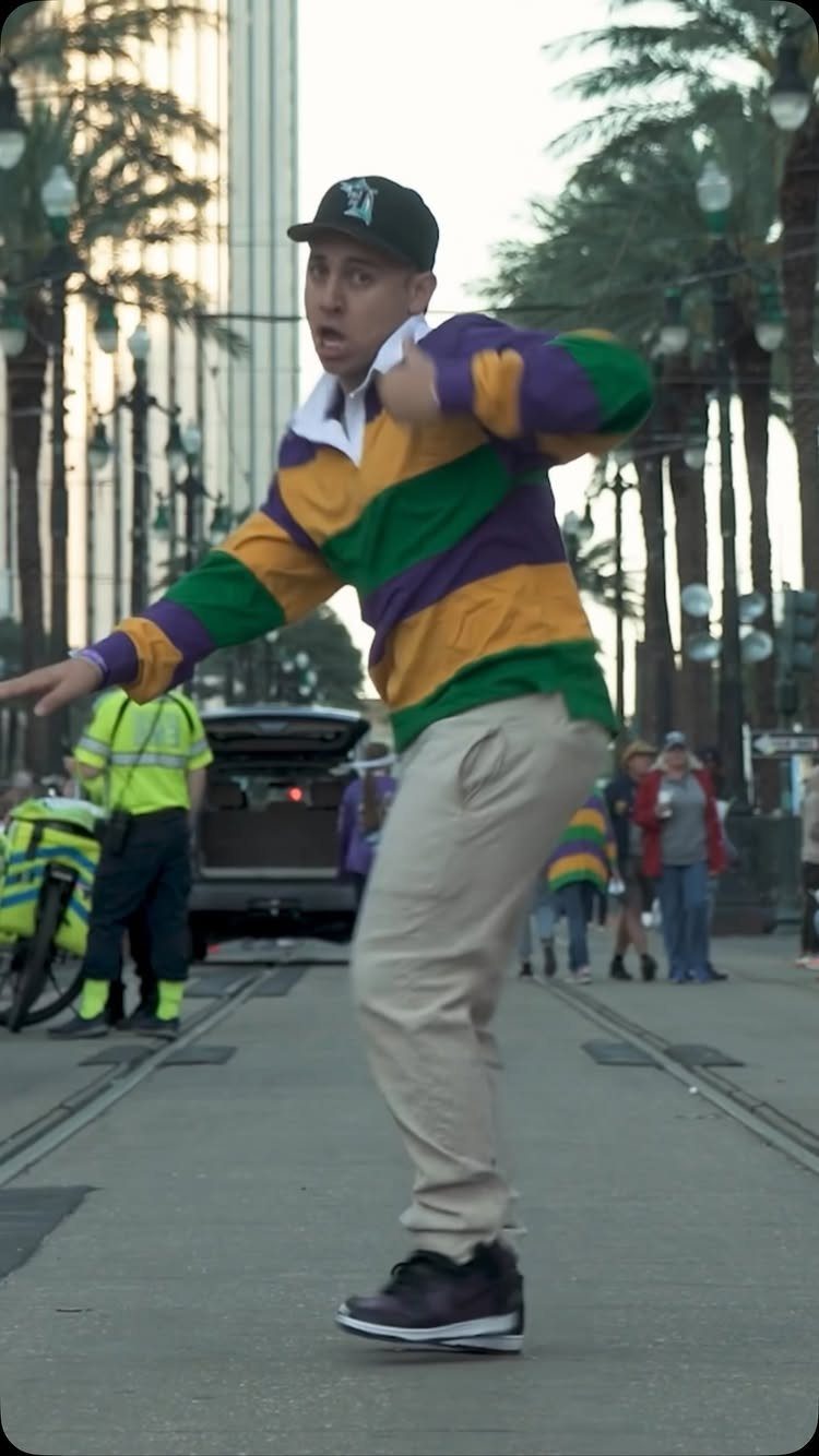 Man in purple, green, and gold striped shirt posing on a city street.