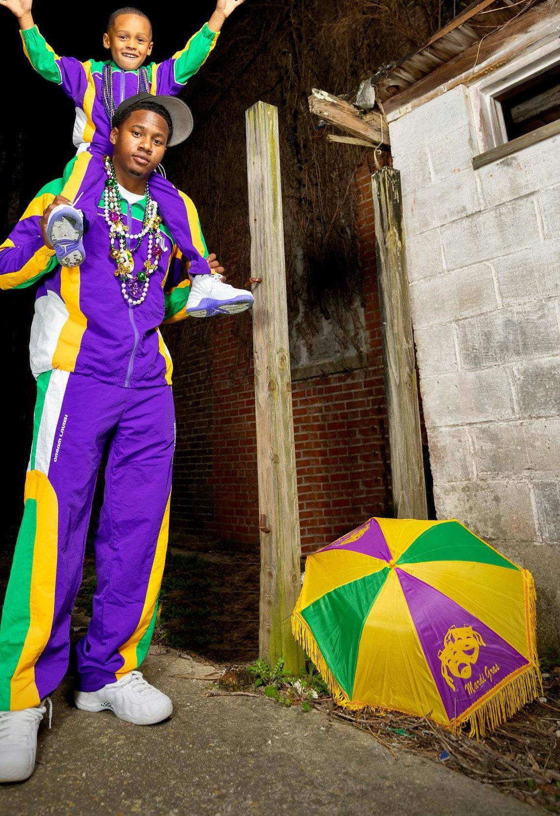 Man and boy in purple, green, and gold tracksuits with Mardi Gras beads.