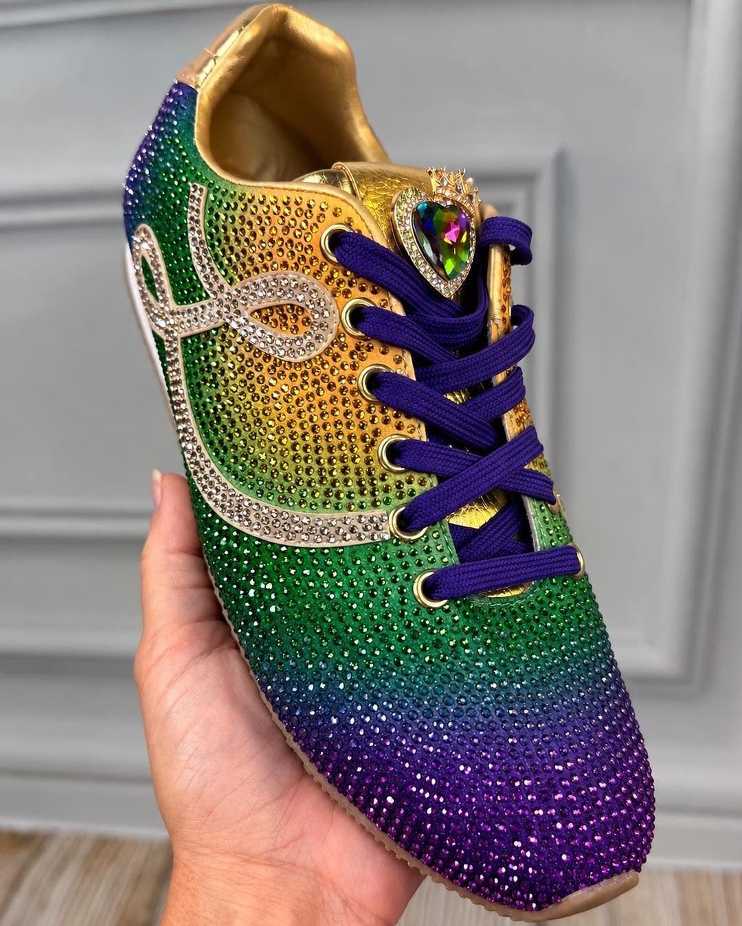 Bejeweled sneaker in purple, green, and gold rhinestones held by a hand.