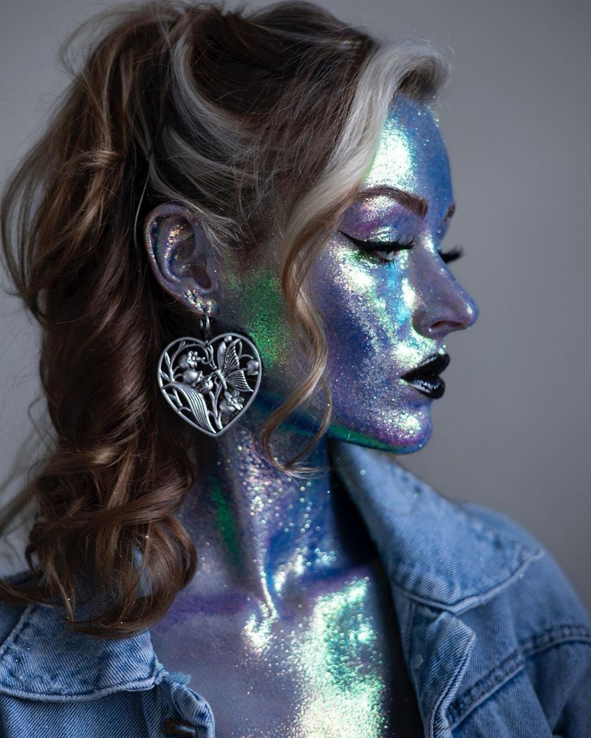 Woman with iridescent blue and green glitter face paint and body glitter.
