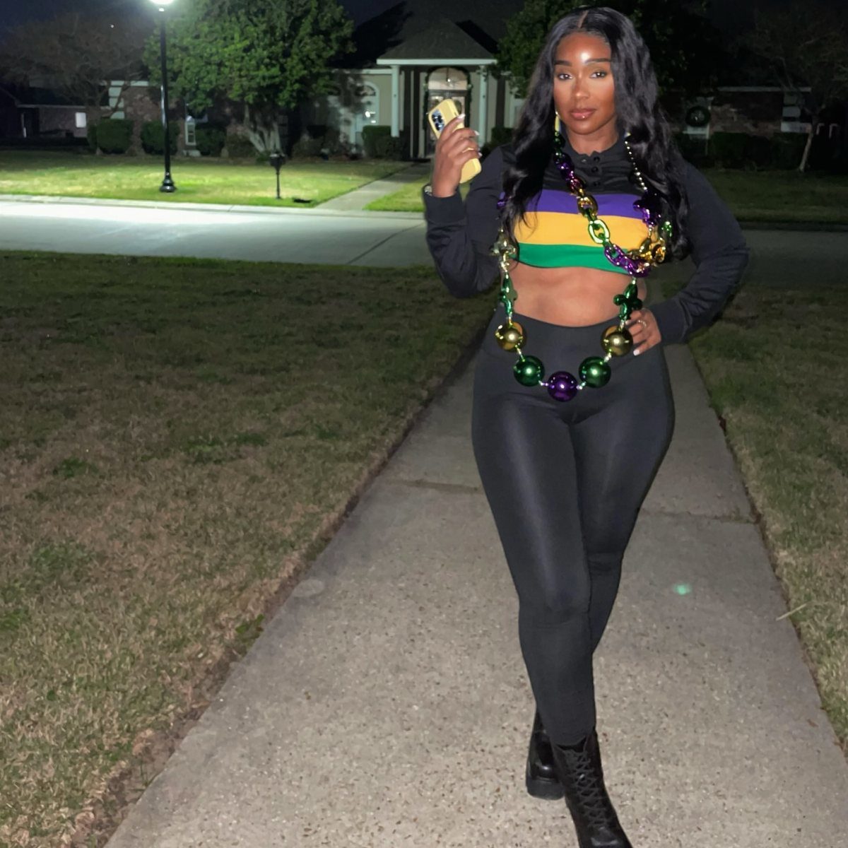 Woman wearing a purple, green, and gold striped crop top and large beads.
