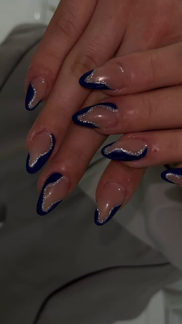 Almond-shaped nails with dark blue French tips and silver glitter accents.
