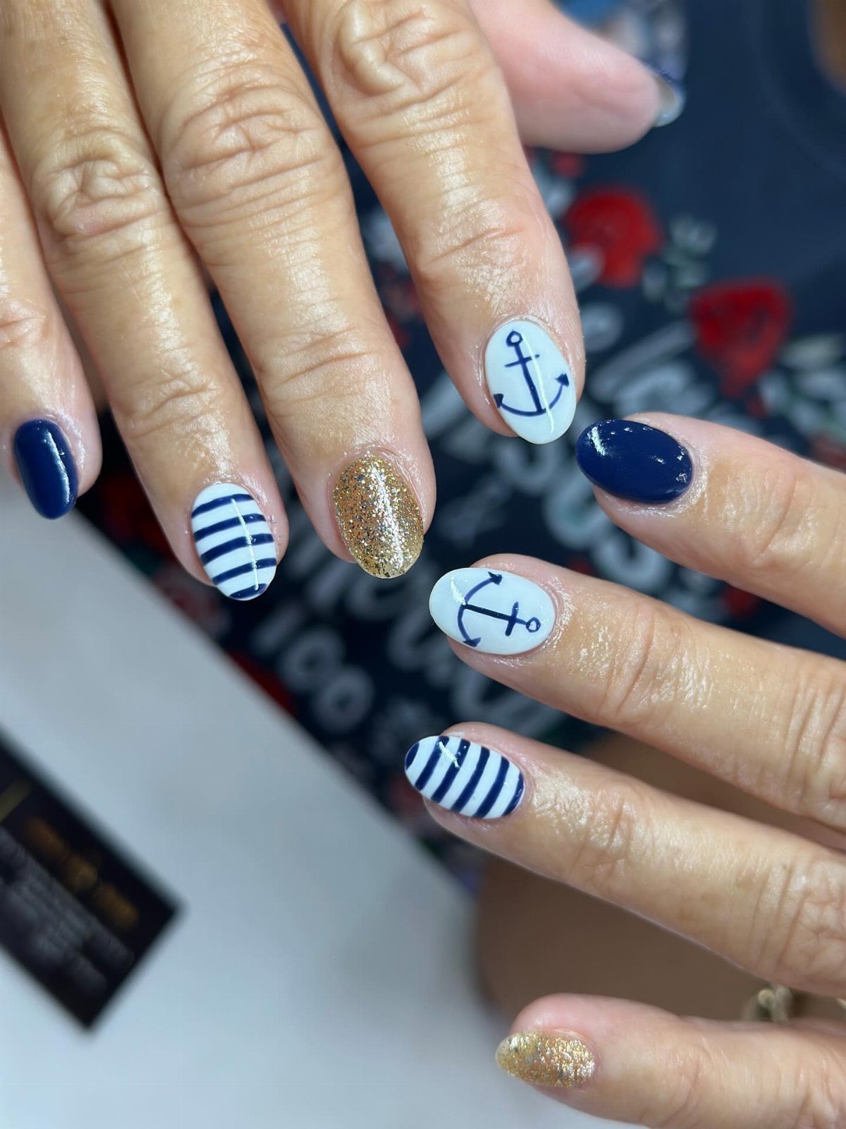 Nautical themed nail art with navy blue, gold glitter, stripes, and anchor designs.