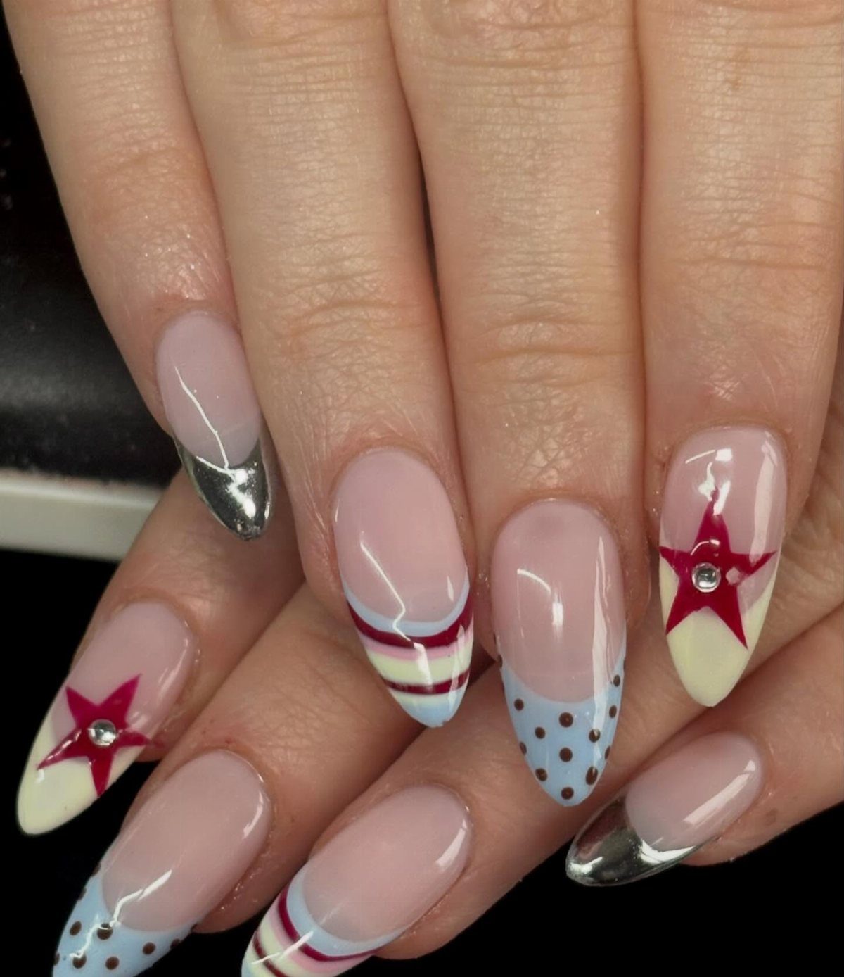 Almond-shaped nails with red stars, blue polka dots, and red and blue stripes.