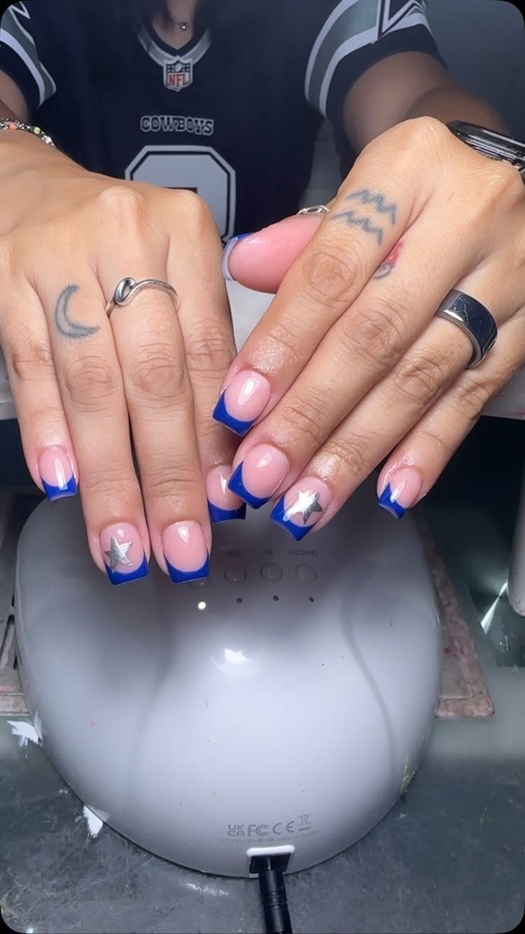 Hands with blue French tip nails and silver stars resting on a nail lamp