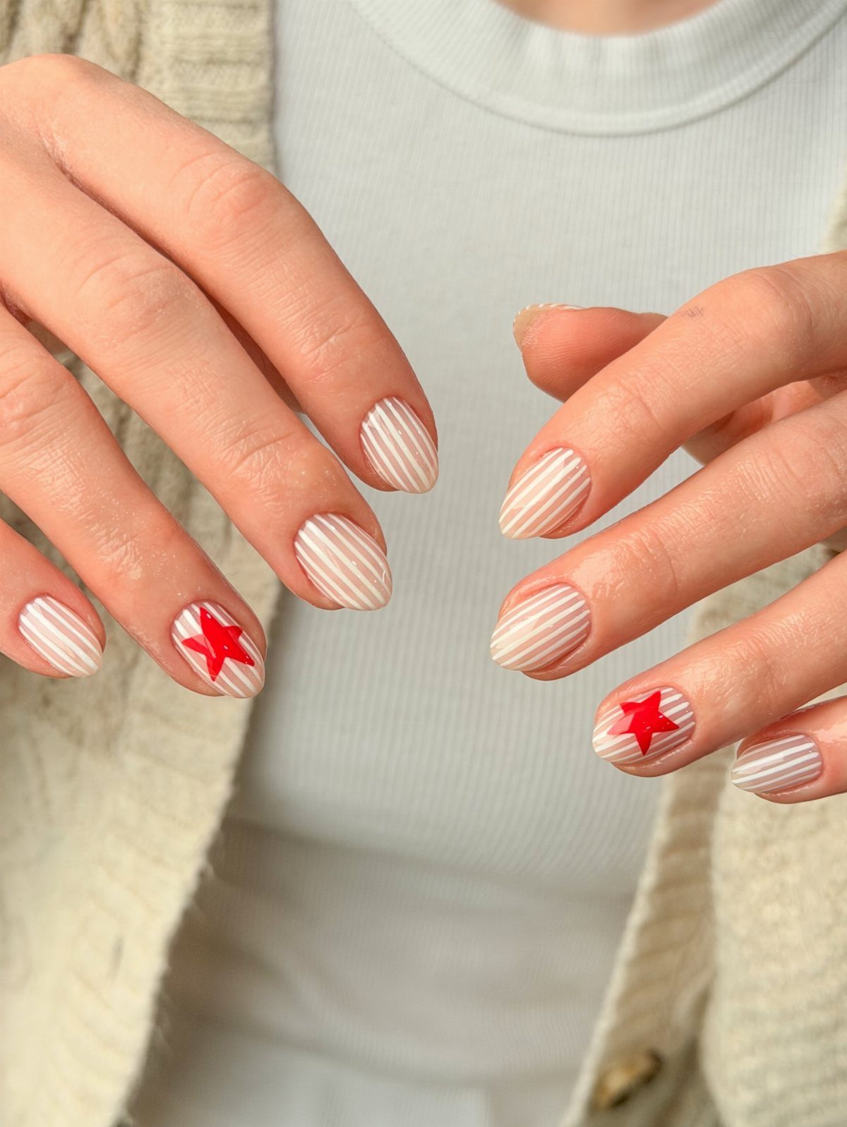 Manicured nails with white and beige stripes and red stars on ring fingers.