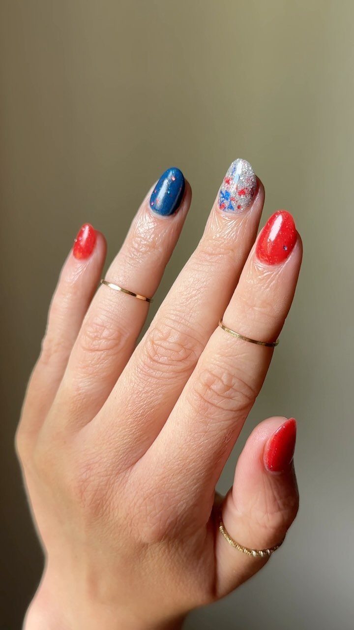 Short nails painted red, royal blue, and speckled white on a hand.