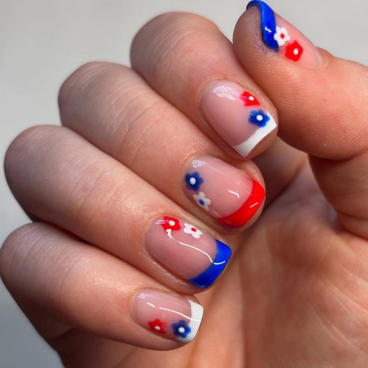 Short nails with red, white, and blue floral art and patriotic French tips.