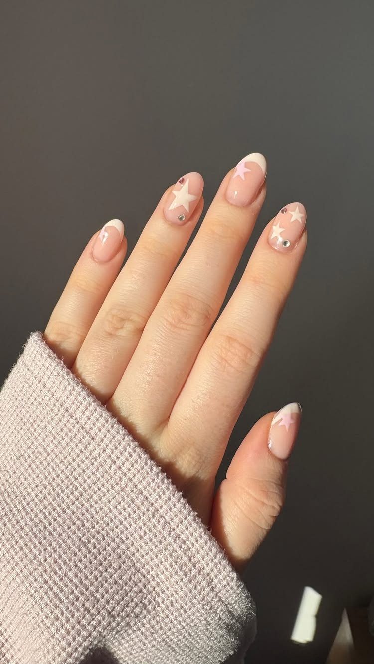 Short nude nails with white star designs and silver rhinestones on a hand.