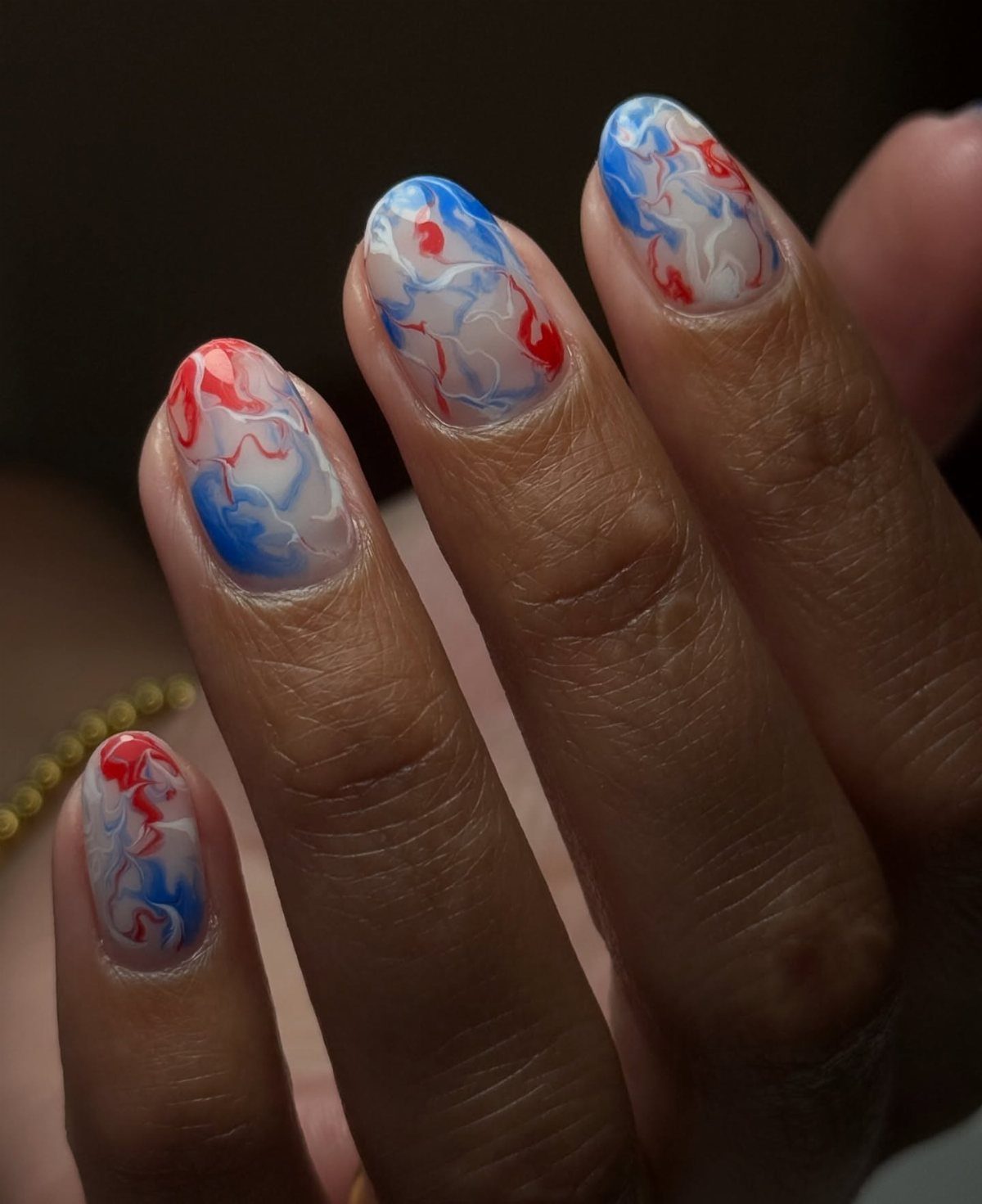 Short nails with a marbled watercolor design in red, white, and blue colors.