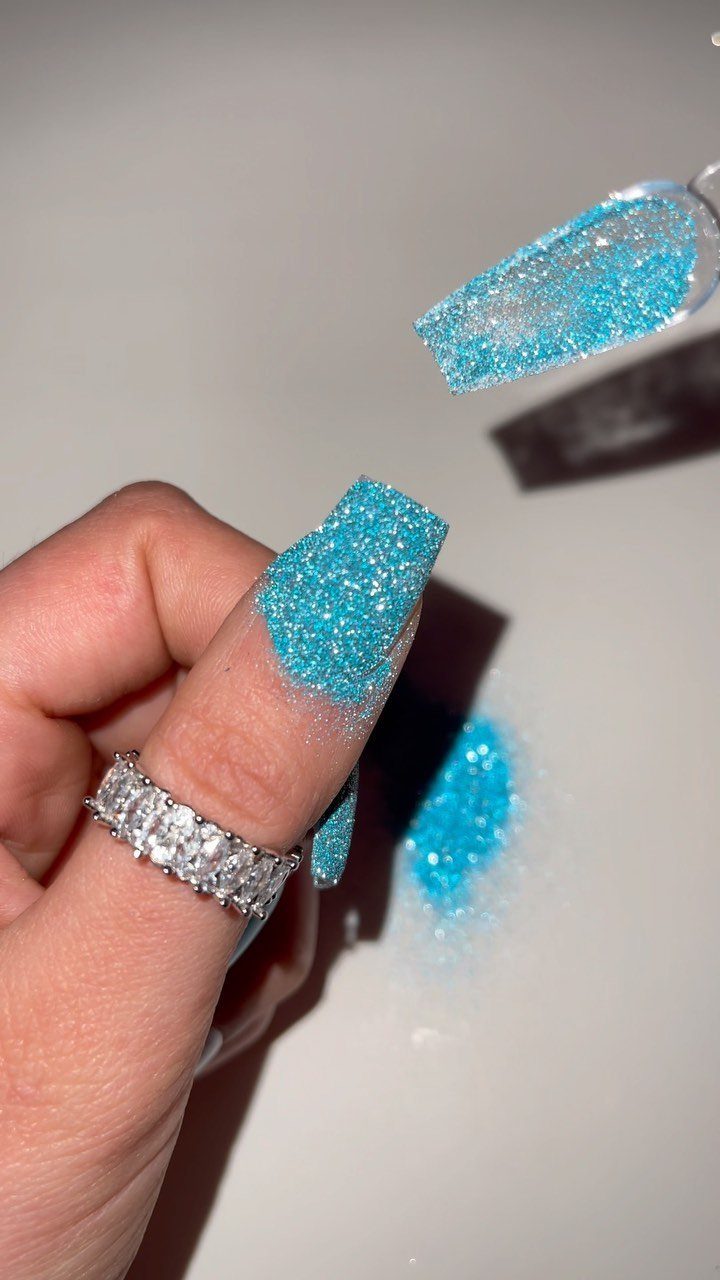 Bright blue glitter nails with a silver diamond ring on a white background
