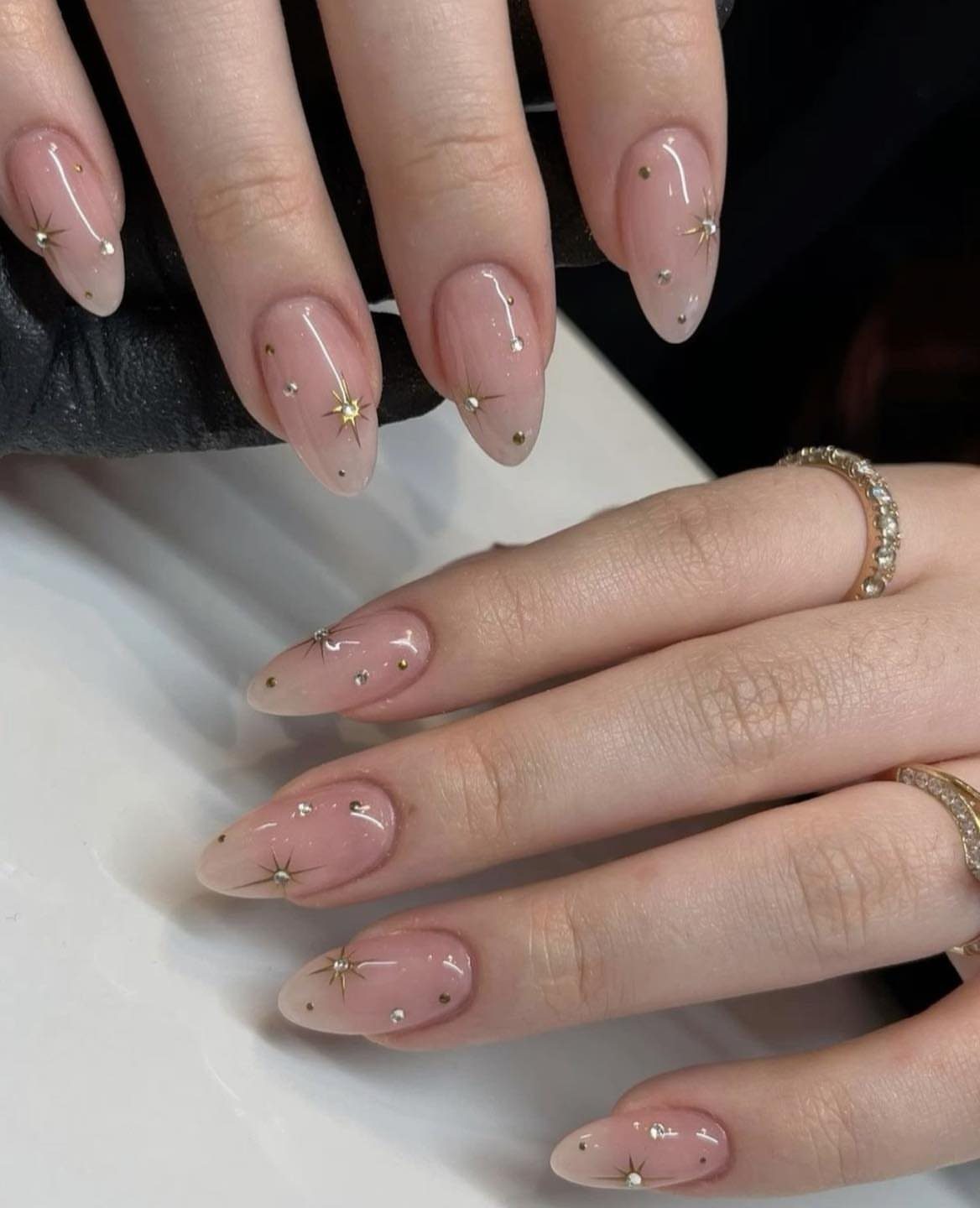 Nude almond-shaped nails decorated with tiny gold stars and small white dots.