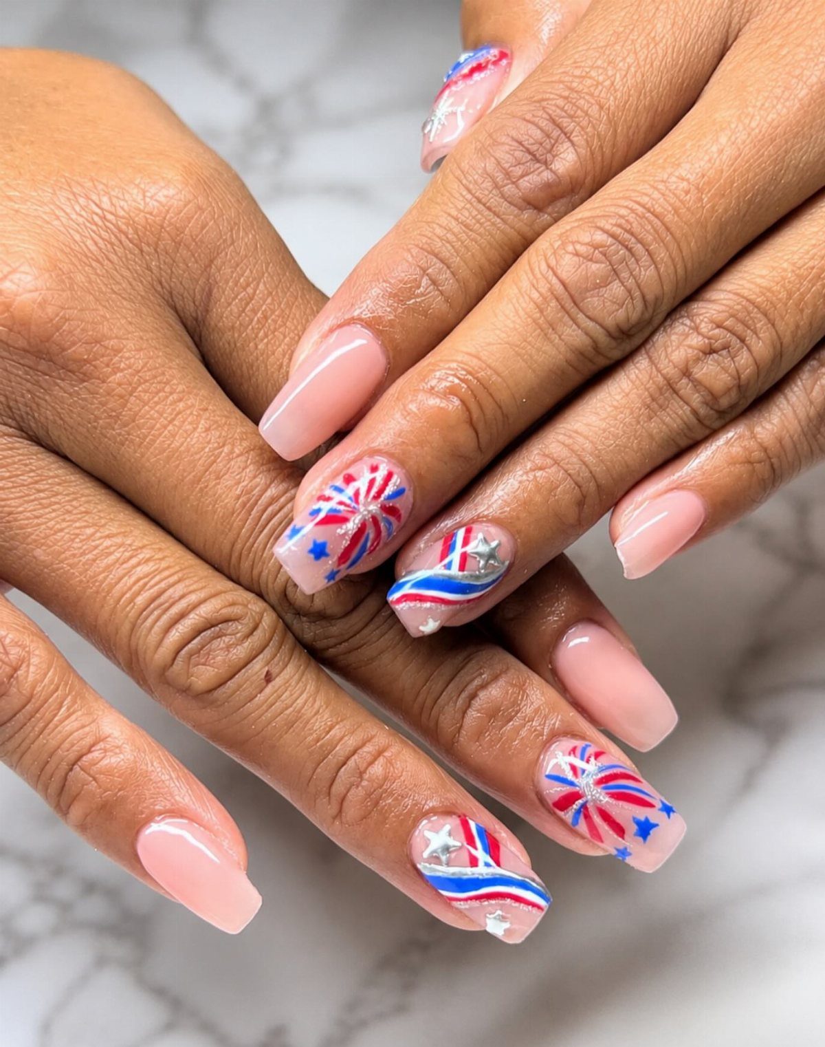 Nails with red, white, and blue starburst firework designs and silver glitter accents.