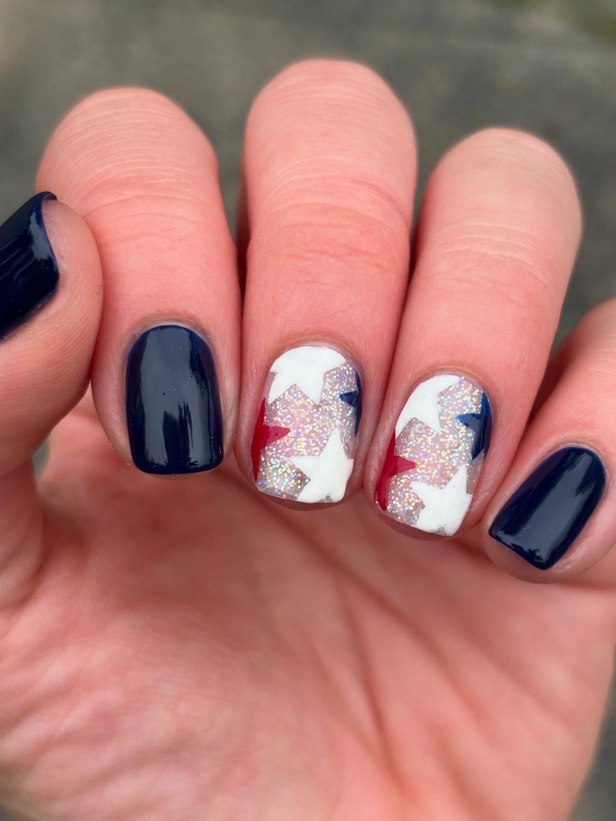 Manicured nails with dark blue polish and white nails featuring red and blue stars.