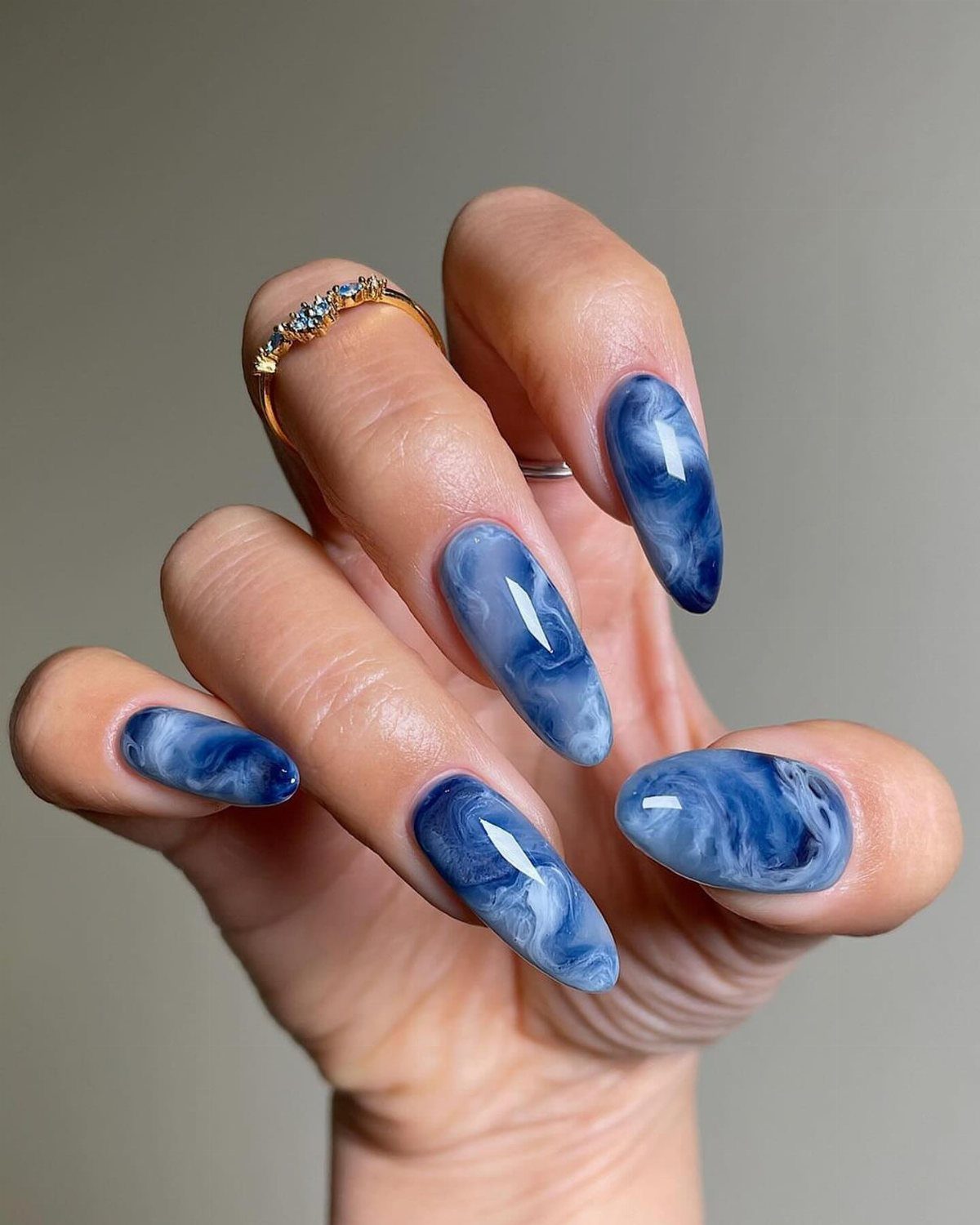 Almond-shaped nails with a blue and white marbled polish effect on a hand.