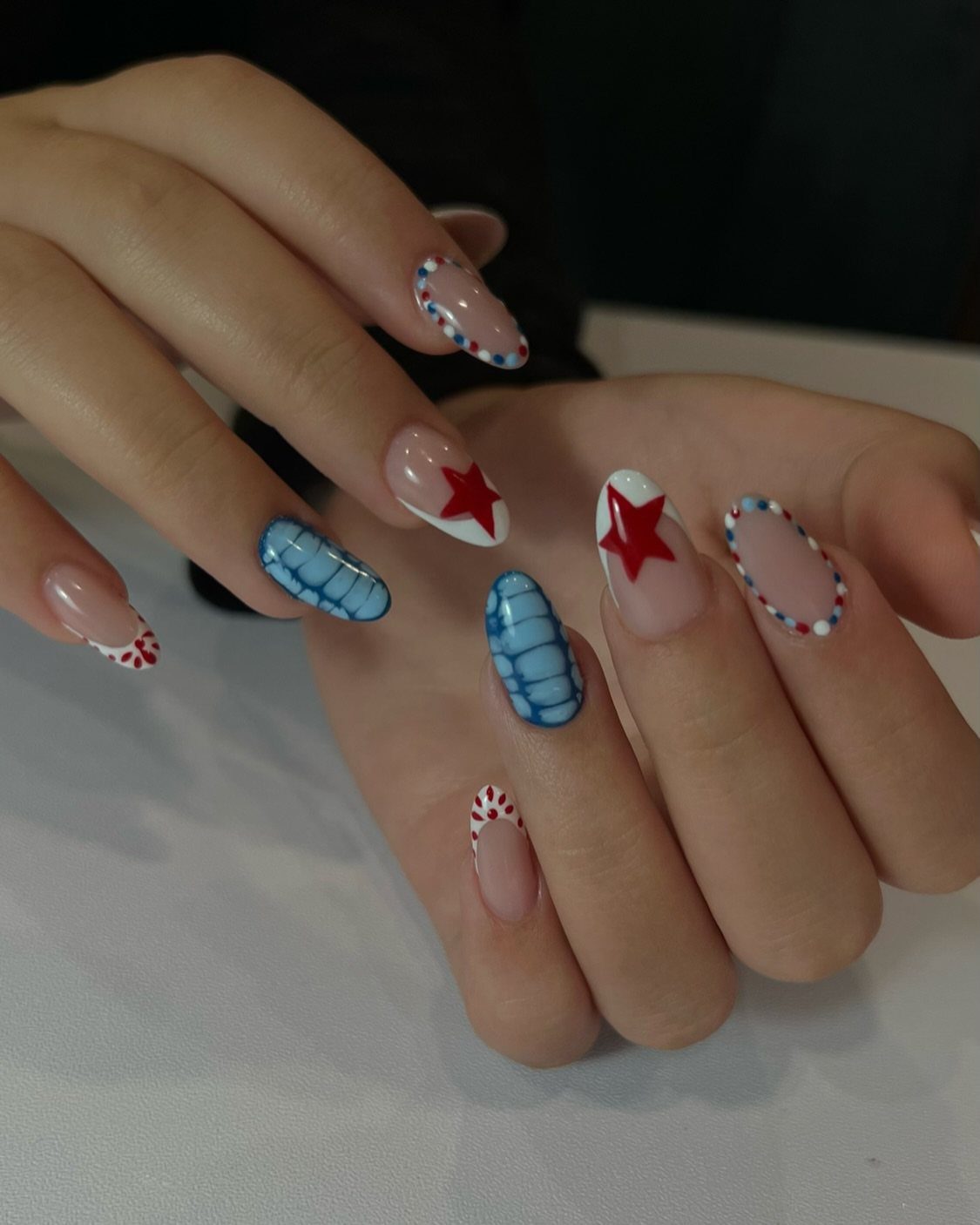 Patriotic almond nails with red stars, blue patterns, and red and white dots.