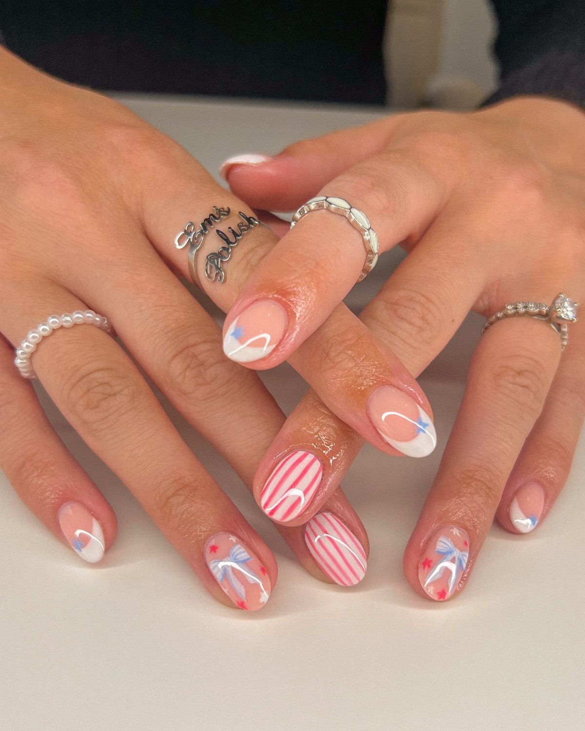 Almond-shaped nails with red, white, and blue patriotic designs and silver rings.