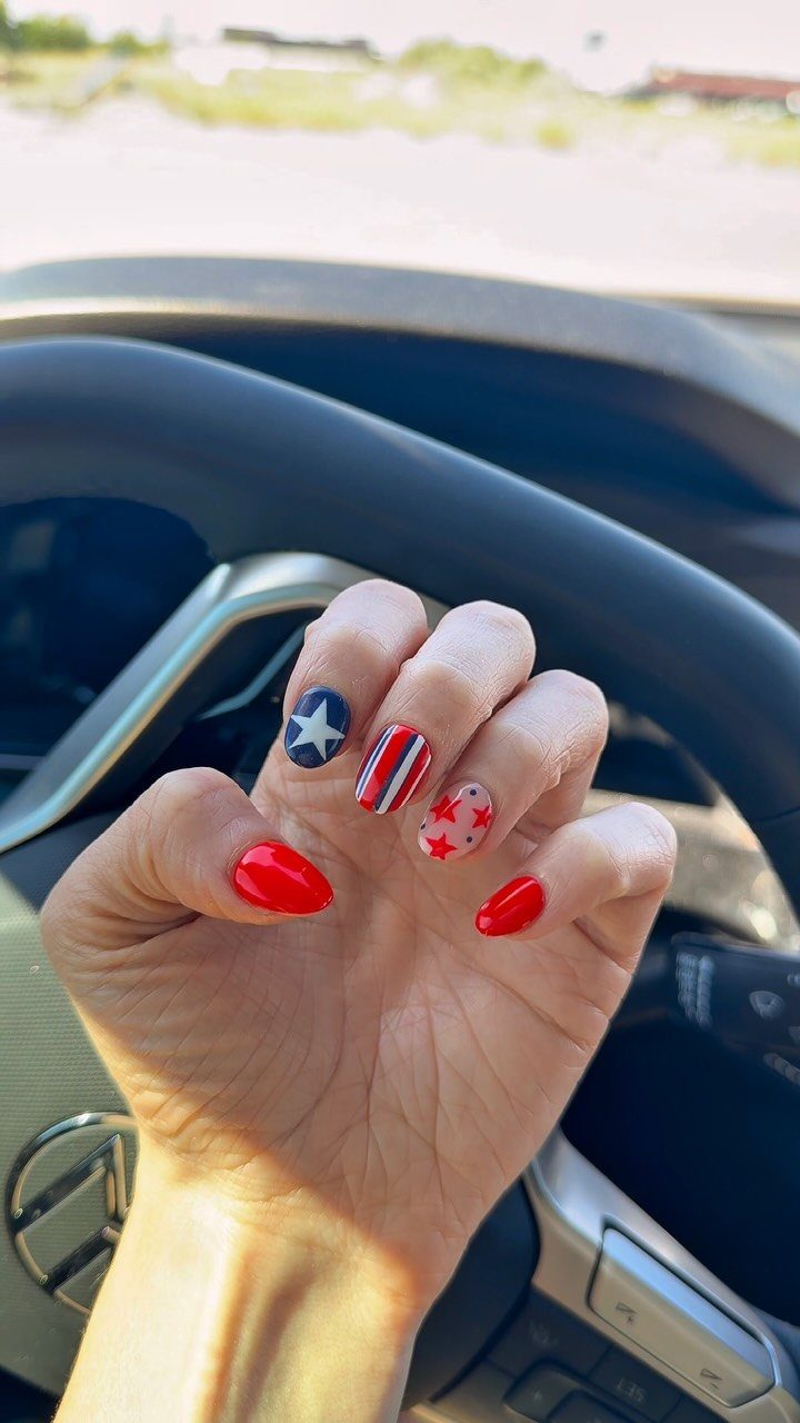 Hand with red, white, and blue patriotic nail art inside a car.