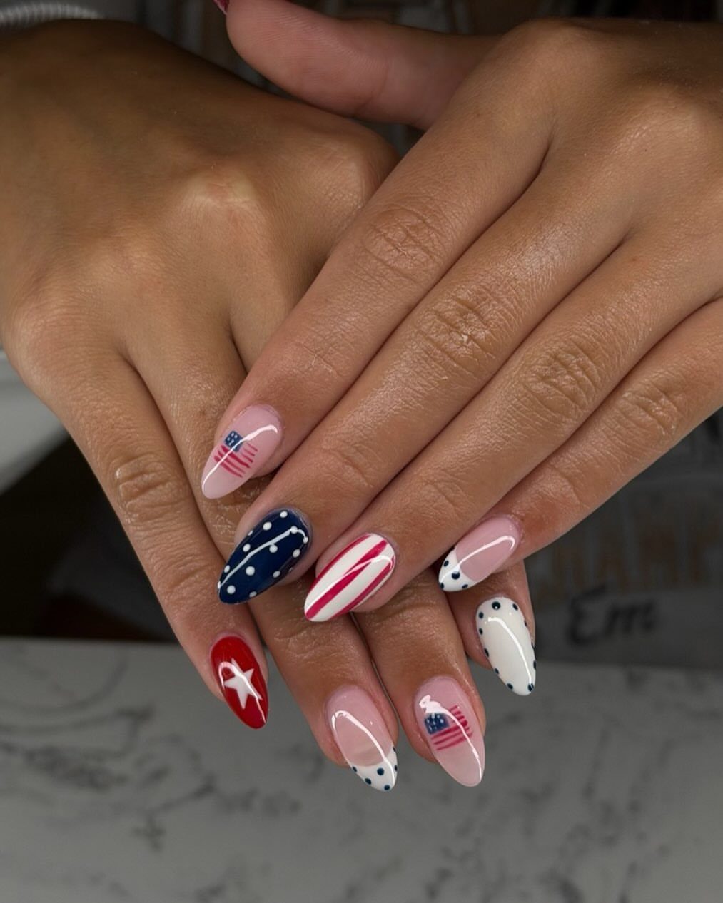 Patriotic almond-shaped nails with red, white, and blue stars and stripes designs.